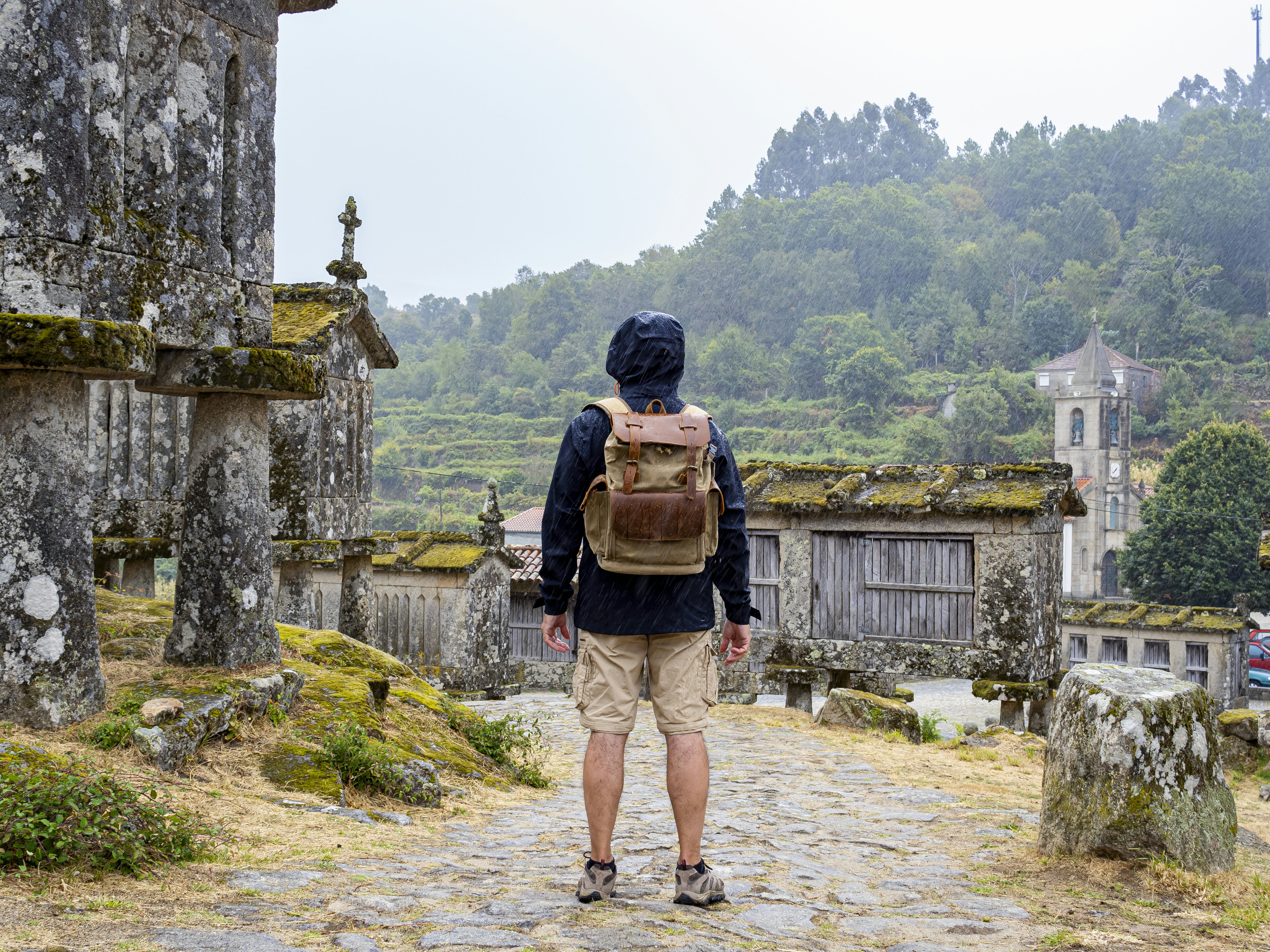 Man on his back looking at the historic stone barns in the town of Lindoso in Portugal as it rains.