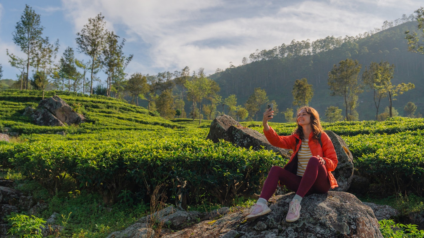A woman taking photos with her phone in a tea plantation in Sri Lanka.
