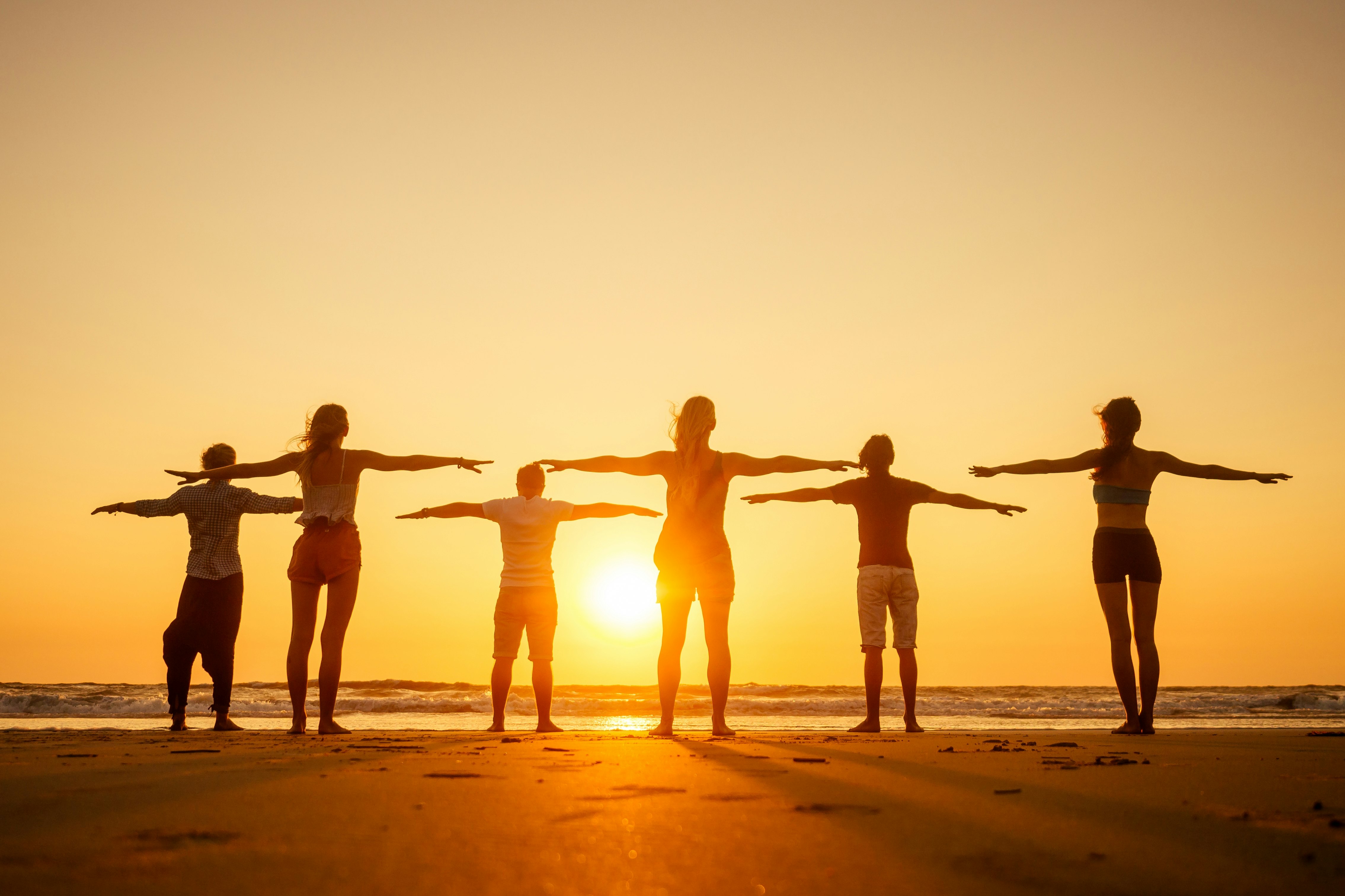 People practicing yoga at dawn on a beach in Goa, India.