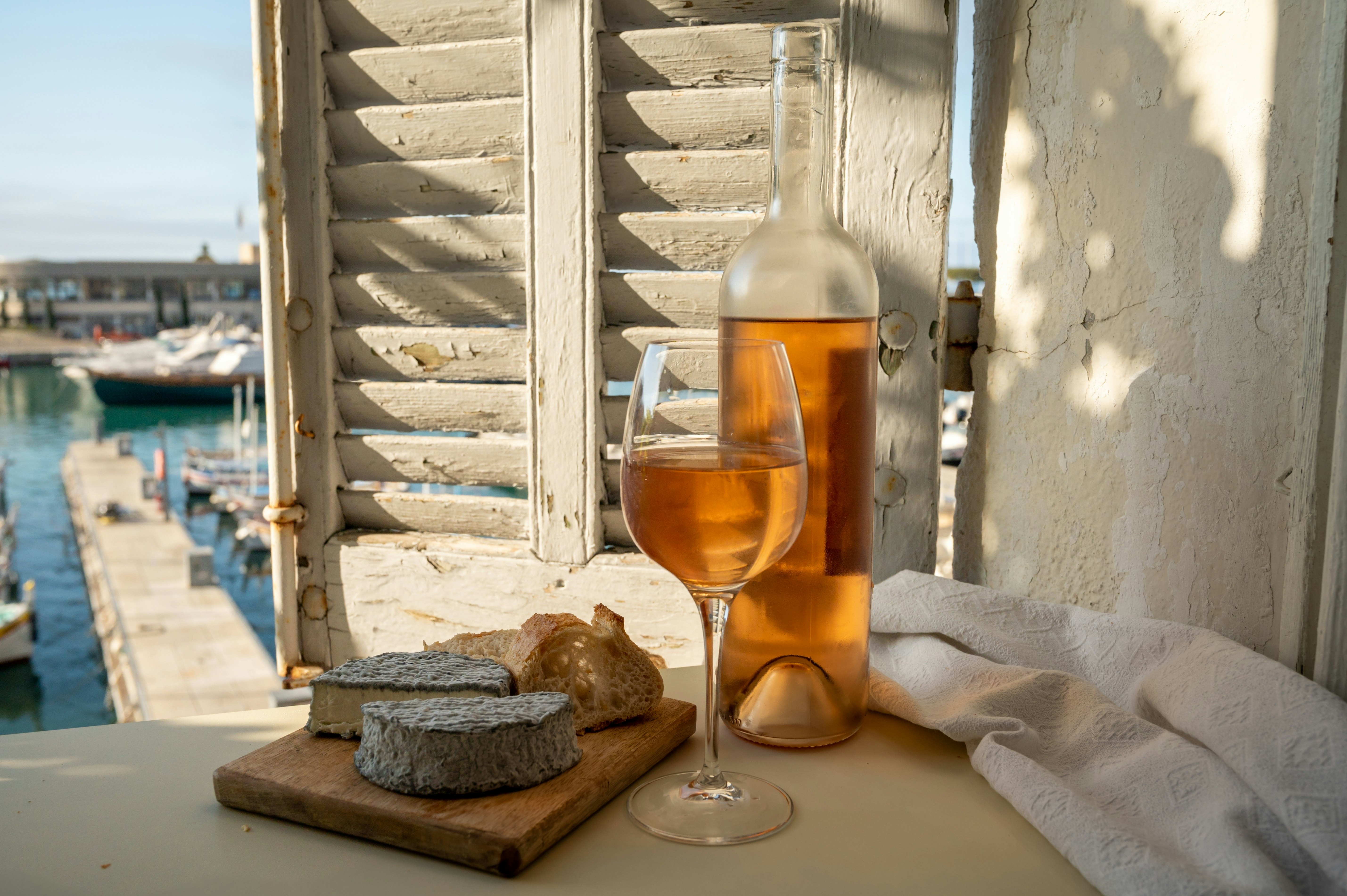 Cold rose Provençal wine in glass and bottle served with goat cheeses on outdoor terrace with view on old fisherman's harbour with colourful boats in Cassis, Provence, France