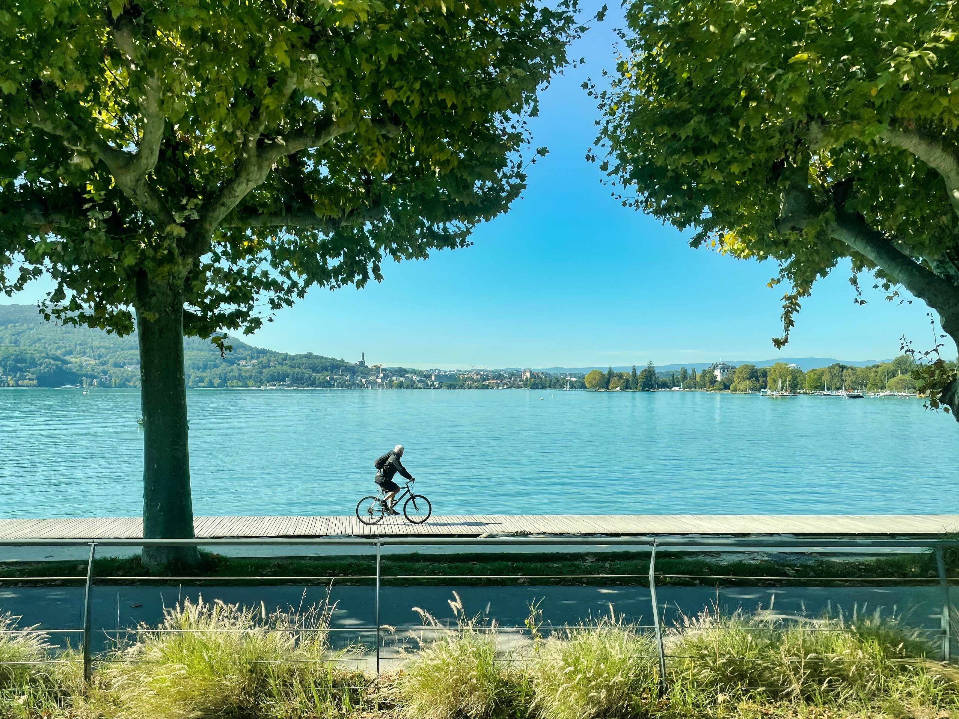 A cyclist is riding on his bicycle along a path by a blue alpine lake.